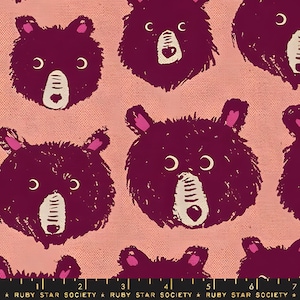 May include: Pink fabric with a repeating pattern of dark purple bear faces. Each bear has white and beige features, including a heart-shaped nose. The ears are pink. The text "RUBY STAR SOCIETY" is at the bottom.