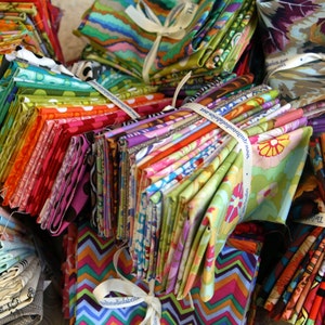May include: A large stack of colorful fabric scraps tied with white ribbon. The fabric is in various patterns and colors, including floral, geometric, and abstract designs.