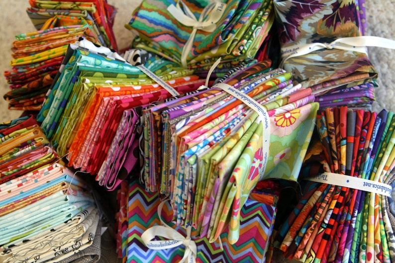 May include: A large stack of colorful fabric scraps tied with white ribbon. The fabric is in various patterns and colors, including floral, geometric, and abstract designs.