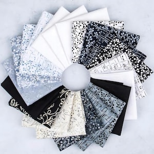 May include: A collection of folded fabric squares arranged in a circular pattern. The fabrics feature a variety of patterns, including floral and geometric designs, in shades of white, black, and gray. The fabrics are likely cotton or a similar material.