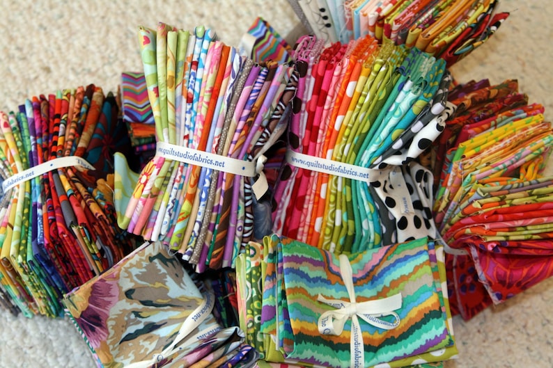May include: A collection of colorful fabric scraps bundled together with a white ribbon and a label that reads "www.quiltstudiofabrics.net".