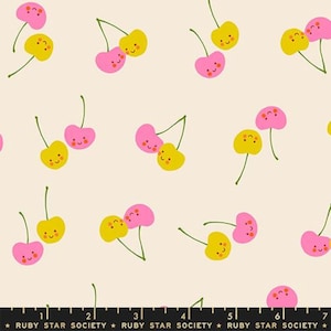 May include: A light cream fabric featuring a repeating pattern of smiling pink and yellow cherries with green stems. A black ruler at the bottom shows measurements in cm, with the text RUBY STAR SOCIETY printed repeatedly along the edge.
