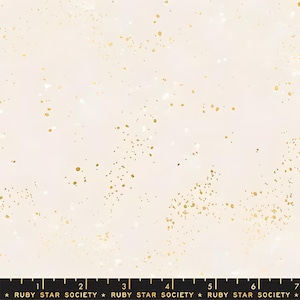 Op de afbeelding: Crèmekleurige stof met een gespikkeld patroon van gouden en witte stippen. De stof heeft een subtiel, aquarelachtig effect, waarbij de gouden stippen in grootte en dichtheid variëren. De onderkant van de afbeelding heeft een zwarte liniaal met de tekst "RUBY STAR SOCIETY".