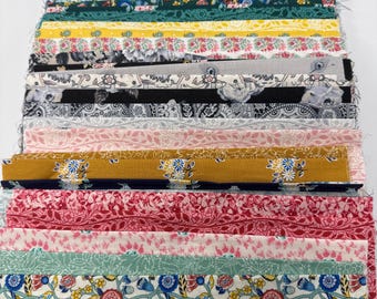 May include: A stack of rectangular fabric strips featuring a variety of floral and botanical patterns in colors including red, blue, yellow, green, pink, black, and white. The fabric pieces are layered neatly, showcasing diverse prints.