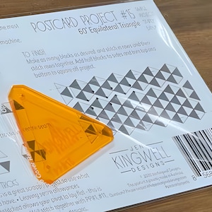 May include: A translucent orange acrylic 60-degree equilateral triangle quilting template placed on top of a Jen Kingwell Designs Postcard Project #15 instruction sheet, which features a printed diagram of a geometric triangle pattern and a barcode.