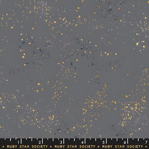 May include: A fabric with a dark gray background, speckled with gold, navy, and white dots. The fabric has a subtle, textured appearance. The text "RUBY STAR SOCIETY" is printed at the bottom.