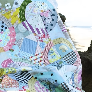 Può includere: Una trapunta patchwork con segmenti di tessuto circolari e geometrici in vari colori e motivi, inclusi disegni floreali, a pois, a righe e a fungo. Il testo HALO PATTERN & ACRYLIC TEMPLATES BY JEN KINGWELL è visibile.