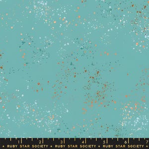 Op de afbeelding: Een talingkleurige stof met een verspreid patroon van kleine, onregelmatige stippen in wit, lichtblauw en metallic koper. Een zwarte liniaal aan de onderkant toont de tekst RUBY STAR SOCIETY, met markeringen tot 18 cm.