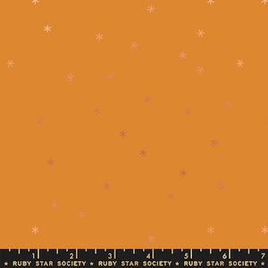 Puede incluir: Tela de color mostaza con un patrón de pequeños copos de nieve rosa pálido. El texto "RUBY STAR SOCIETY" está impreso en la parte inferior de la imagen.