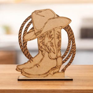 Puede incluir: Decoración de madera con temática de vaquero que presenta un sombrero, botas y un diseño de cuerda. Las botas y el sombrero están intrincadamente cortados de madera y se apoyan en una base rectangular. La cuerda forma un marco circular.