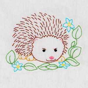 May include: Embroidered design of a hedgehog with brown quills, a white face, and a pink nose. The hedgehog is surrounded by green leaves and blue flowers, all stitched on a white background. The design has a whimsical, handmade feel.