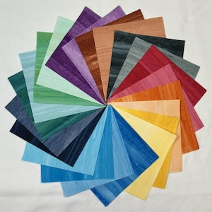 May include: A circular arrangement of colorful, square-shaped pieces of paper. The papers display a variety of colors, including shades of blue, green, purple, red, orange, and yellow. Each piece has a unique wood grain pattern, creating a visually appealing display.