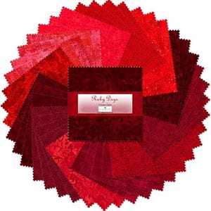 May include: A circular stack of red fabric squares in varying shades, from light pink to deep burgundy. The fabric has different patterns, including floral and dotted designs. The label in the center reads "Ruby Days".