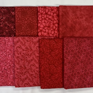 May include: A collection of eight fabric squares in various shades of red. The fabrics feature diverse patterns, including floral, swirling, and textured designs. The color palette ranges from deep burgundy to lighter, rosy hues.