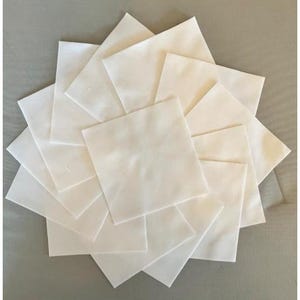 May include: A collection of white square napkins arranged in a circular pattern. The napkins are made of a soft, possibly linen or cotton material, and are neatly folded. The arrangement creates a visually appealing, symmetrical design, suitable for table settings or crafts.