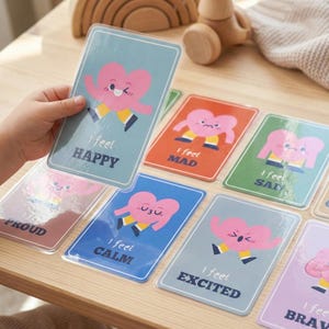 May include: A collection of emotion flashcards with a heart character. Each card features a different emotion, such as "Happy," "Mad," and "Calm." The cards are in various colors, including blue, orange, and green, with the text "I feel" above each emotion.