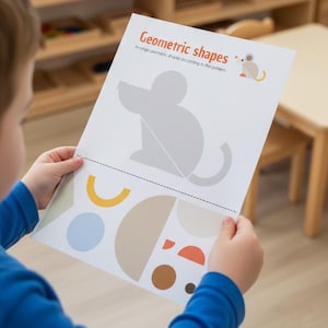 Może przedstawiać: Dziecko trzyma kartę pracy zatytułowaną "Kształty geometryczne". Karta pracy zawiera szarą sylwetkę myszy i różne kształty geometryczne w kolorze żółtym, niebieskim, brązowym i pomarańczowym. Tło obejmuje drewniane półki i stół.