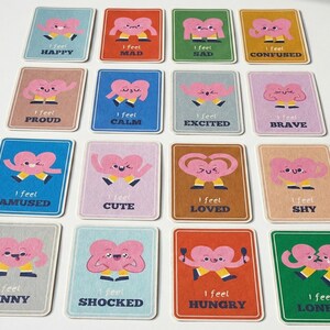 May include: A collection of colorful emotion cards. Each card features a pink heart character with arms and legs, expressing different feelings. The cards have text such as "I feel happy," "I feel sad," and "I feel loved."