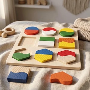 Può includere: Puzzle di forme in legno con nove pezzi geometrici colorati. I pezzi sono rossi, blu, verdi, gialli e arancioni. Il puzzle è progettato per bambini ed è realizzato in legno naturale.