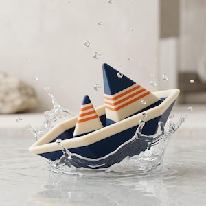 Könnte beinhalten: Ein marineblaues und cremefarbenes Spielzeugboot mit zwei dreieckigen Segeln, die mit horizontalen orangefarbenen Streifen versehen sind. Das Boot befindet sich im Wasser mit einem sichtbaren Spritzwassereffekt um den Rumpf.