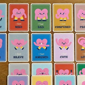 May include: A collection of emotion cards featuring pink heart characters with various expressions. Each card has a different background color and text such as "I feel Happy", "I feel Mad", and "I feel Loved".