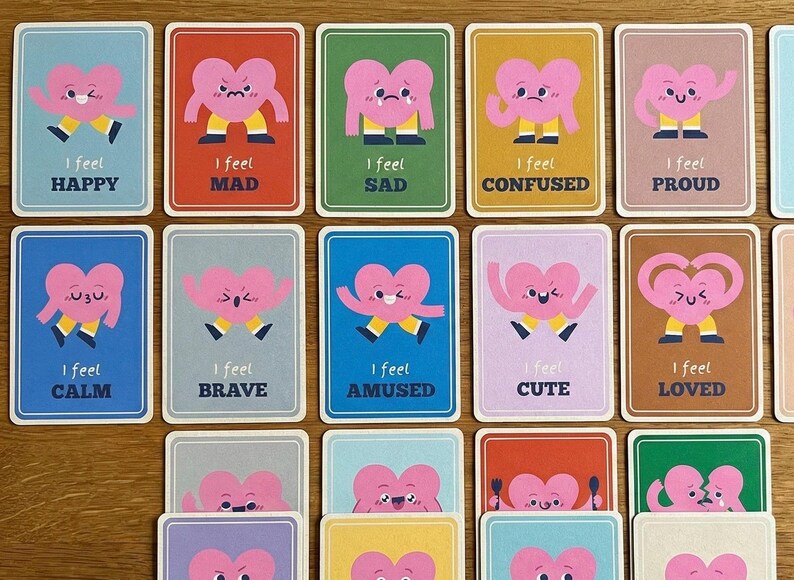 May include: A collection of emotion cards featuring pink heart characters with various expressions. Each card has a different background color and text such as "I feel Happy", "I feel Mad", and "I feel Loved".