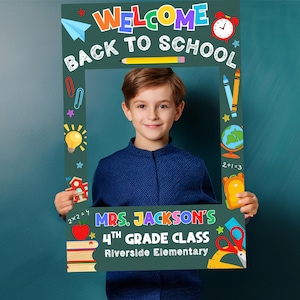 以下が含まれることがあります： カラフルな文字で「WELCOME BACK TO SCHOOL」と書かれたフォトフレーム。フレームには学校をテーマにしたイラストと「MRS. JACKSON'S 4TH GRADE CLASS Riverside Elementary」の文字が入っています。若い男の子がフレームを持っています。