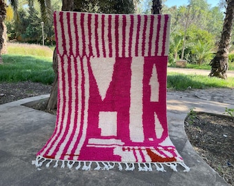 May include: A pink and white striped rug with a geometric design. The rug has a fringe border.