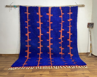 May include: A vibrant blue rug with a repeating pattern of orange vertical lines. The rug has a thick, textured pile and a fringe along the bottom edge. It is displayed against a neutral background, showcasing its bold design.
