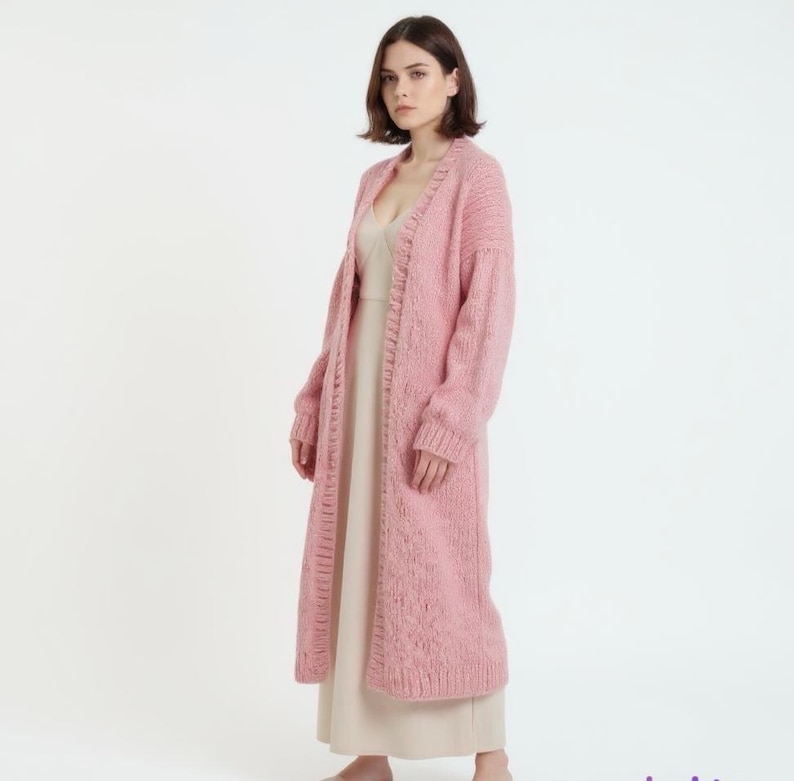 A long pink knitted cardigan on a woman over a light dress.