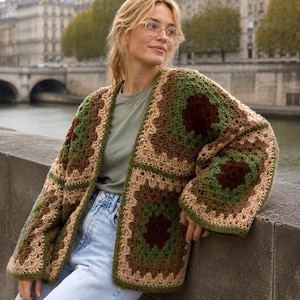 Può includere: Un cardigan a maniche lunghe aperto sul davanti, realizzato con diversi quadrati all'uncinetto tipo granny square. Il capo presenta una palette di colori marrone scuro, verde bosco e beige, con un motivo testurizzato a maglia aperta.