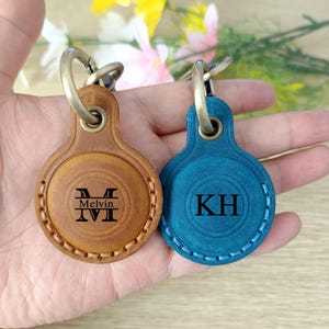 May include: Two leather keychains with metal rings. One is tan with the name "Melvin" and the initials "MVI" engraved. The other is teal with the initials "KH" engraved. Both have a stitched border.