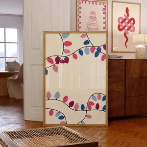 May include: A framed print of a string of pink and blue lights on a cream background. The lights are arranged in a wavy pattern. The print is hanging on a wall in a room with a wooden floor and a wooden dresser.
