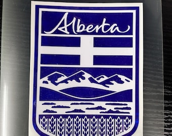 May include: A blue and white sticker featuring the word "Alberta" in cursive script. The design includes a shield shape with a cross, mountains, and wheat stalks, representing the province of Alberta, Canada.