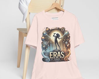 May include: Pink t-shirt with a graphic of a woman singing on a stage with the text "The Eras Tour" in gold lettering.