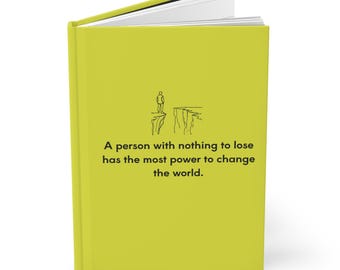 May include: A yellow journal with a black and white illustration of a person standing on a cliff. The journal has the text "A person with nothing to lose has the most power to change the world."