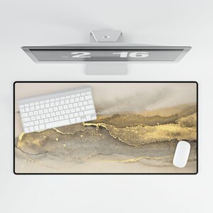 Könnte beinhalten: Eine beige und goldene abstrakte Schreibtischunterlage mit einer weißen Tastatur und einer weißen Maus. Die Unterlage hat ein marmorartiges Design mit goldenen Akzenten.