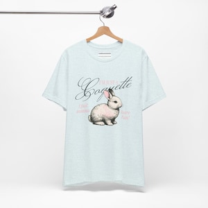 Pode incluir: Uma camiseta azul clara com um gráfico de um coelho branco com orelhas cor-de-rosa e o texto "I'm just a Caguette I just wanna have fun!"