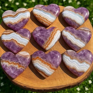 May include: Nine heart-shaped amethyst stones with unique patterns of white, brown, and purple hues. The polished stones are arranged on a wooden surface, showcasing their natural beauty and variations in color and texture.