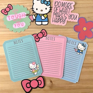 May include: Three lined paper notepads with Hello Kitty characters and the word "NOTES" at the top. The notepads are blue, pink, and light blue. There are also several Hello Kitty stickers with motivational quotes.