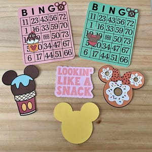May include: Pink and green bingo cards with Mickey Mouse-themed graphics, including ice cream, donuts, and a bow. The cards feature numbers and the word "BINGO." Additional cutouts include a yellow Mickey Mouse head and a pink rectangle with the text "LOOKIN LIKE A SNACK."