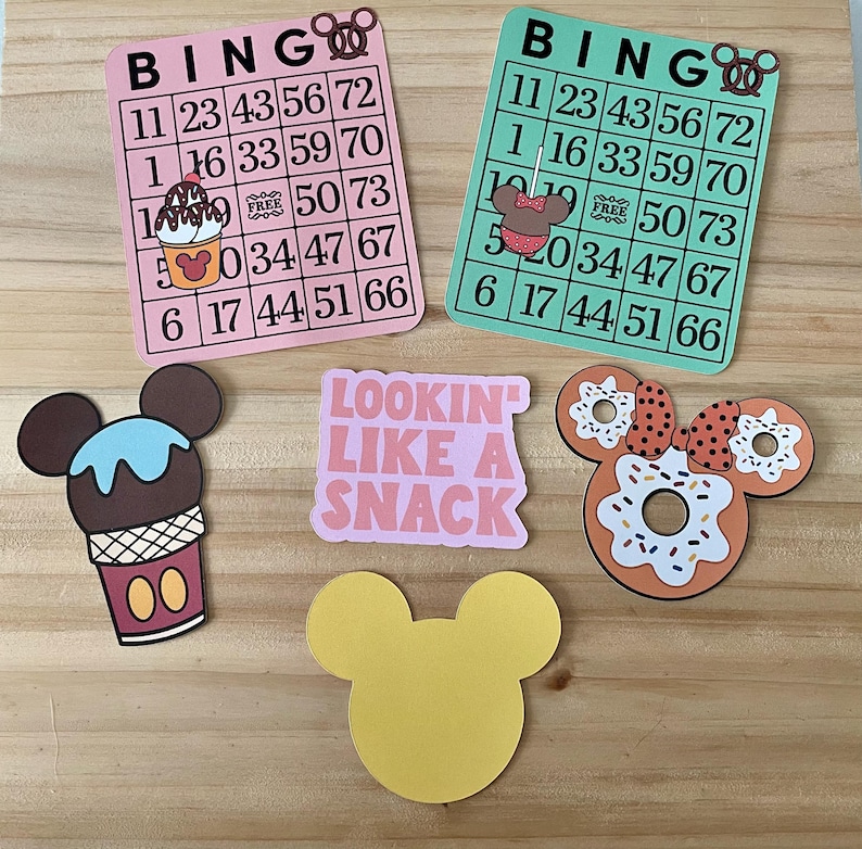 May include: Pink and green bingo cards with Mickey Mouse-themed graphics, including ice cream, donuts, and a bow. The cards feature numbers and the word "BINGO." Additional cutouts include a yellow Mickey Mouse head and a pink rectangle with the text "LOOKIN LIKE A SNACK."