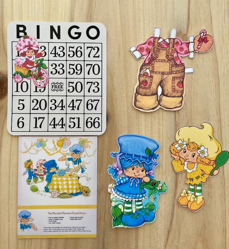 May include: A collection of vintage Strawberry Shortcake themed paper cutouts and a bingo card. The bingo card has the word "BINGO" at the top and numbers in the grid. The cutouts include characters in various outfits and poses.