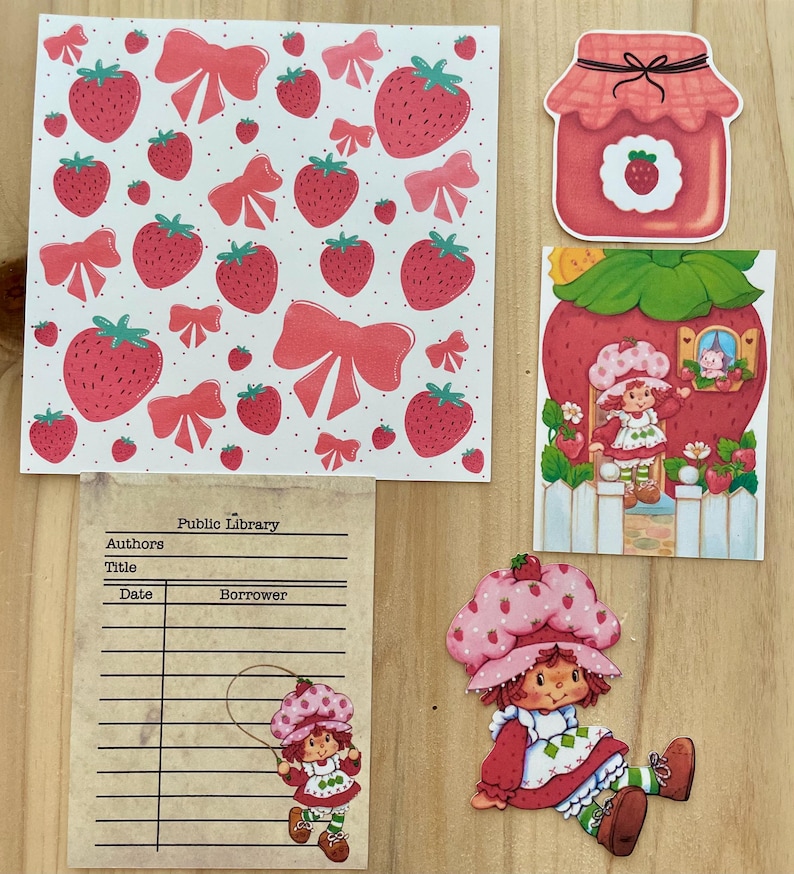 May include: A collection of strawberry-themed paper cutouts and stickers. Includes a pattern of strawberries and bows, a jar of strawberry jam, and several images of a cartoon character in a strawberry hat and dress. A library card is also present.