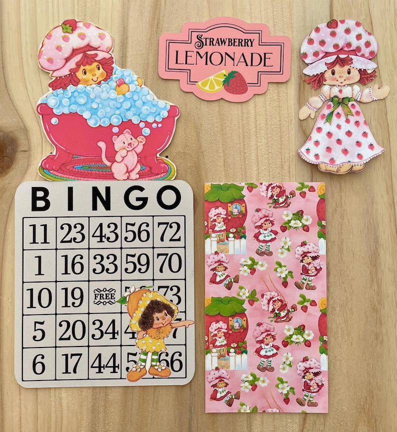 May include: A collection of vintage-style Strawberry Shortcake themed items. Includes a bingo card, a Strawberry Lemonade sign, a patterned paper, and die-cut figures of the character. The color palette is primarily pink, red, and white.
