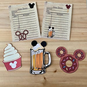 May include: A collection of paper cutouts and library cards with a theme of food and beverages. The cutouts include a soft-serve ice cream, a beer mug, and donuts, all with Mickey Mouse ears. The library cards have the words "Public Library".