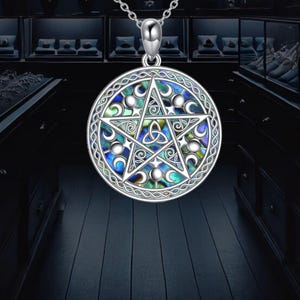 Puede incluir: Collar con colgante plateado con un colgante circular con un diseño de pentagrama. El colgante tiene una incrustación de nácar con detalles azules, verdes y blancos. El collar tiene una cadena delicada.