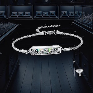 May include: Silver bracelet with a rectangular pendant featuring rose and leaf designs. The pendant has an iridescent abalone shell inlay. A small funnel and tool are included. The bracelet is displayed on a dark surface.