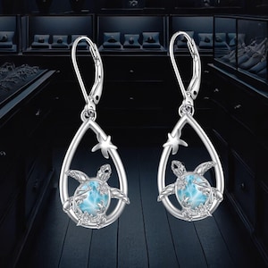 May include: A pair of silver dangle earrings featuring a blue and white sea turtle design with a starfish accent. The earrings are in the shape of a teardrop.
