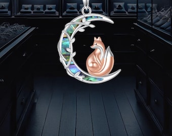 May include: Silver-toned necklace featuring a crescent moon pendant with a rose gold fox inside. The moon is adorned with iridescent abalone shell and delicate leaf accents. A charming piece of jewelry.